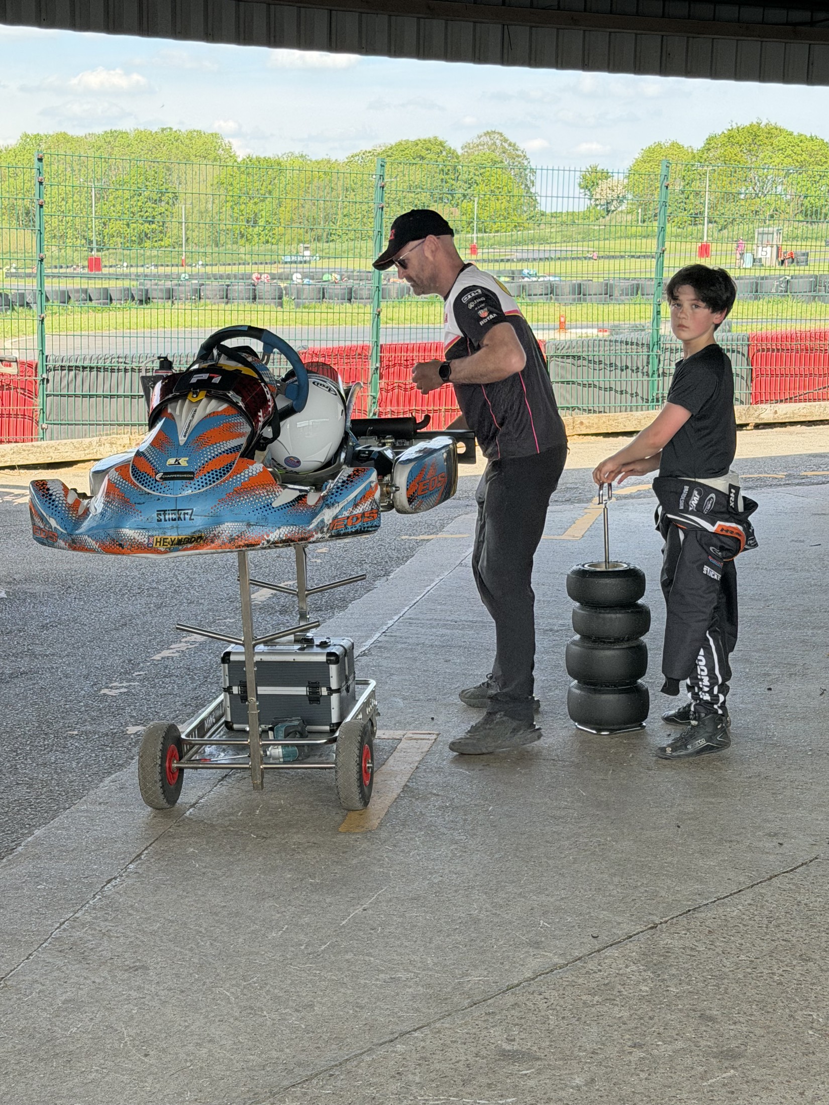 Felix beside his kart while an adult works on its preparation