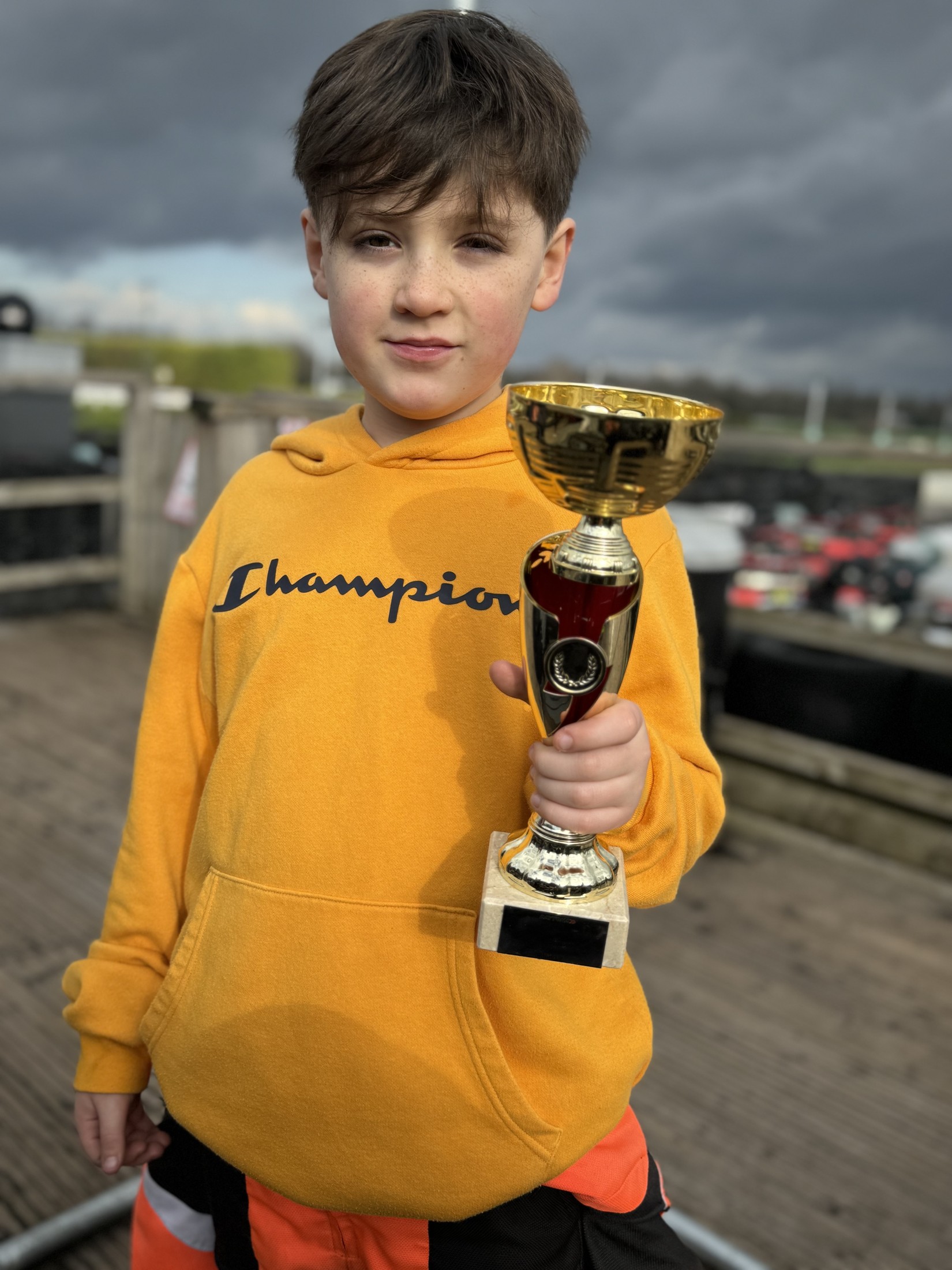 Felix at the circuit in a yellow hoodie holding a gold trophy